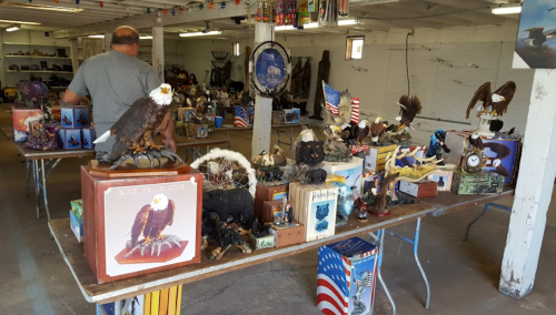 A man browses a collection of eagle figurines and patriotic decor in a spacious indoor market.