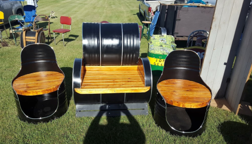Three unique chairs made from barrels, featuring wooden seats and a central bench, set on a grassy area.