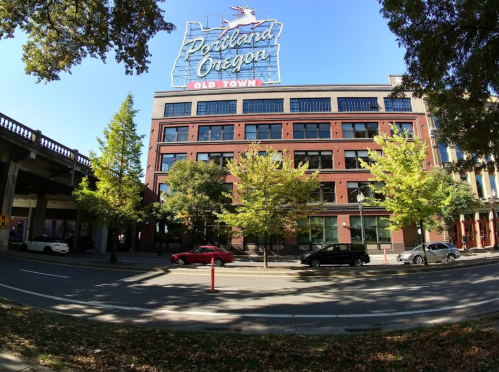 A view of a brick building with a "Portland Oregon Old Town" sign, surrounded by trees and cars on the street.