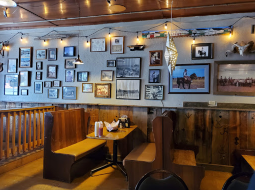 Cozy restaurant interior with wooden booths, a table, and a wall adorned with framed photos and string lights.