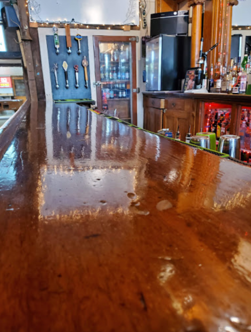 A polished wooden bar top with reflections, featuring taps and a well-stocked back bar in a cozy setting.