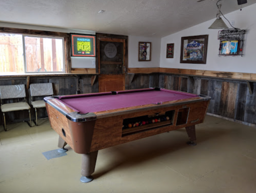A cozy game room featuring a purple felt pool table and rustic wooden walls, with chairs and decor in the background.