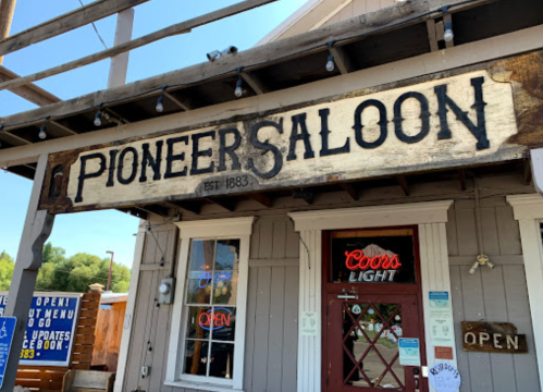 Sign for "Pioneer Saloon" established in 1883, with a rustic exterior and open sign visible.
