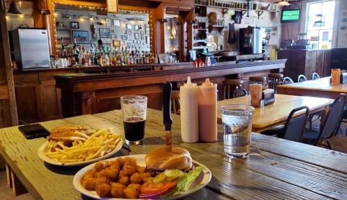 A table with a burger, fries, and fried snacks, with a bar and drinks in the background of a cozy restaurant.