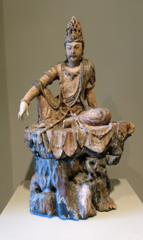 A seated Buddha statue with intricate details, resting on a lotus pedestal, showcasing serene expression and ornate attire.
