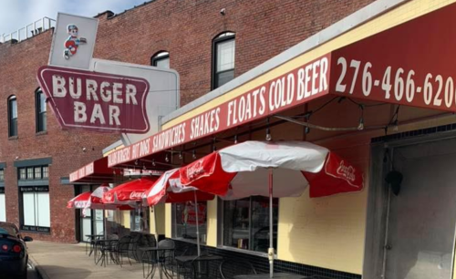 Exterior of Burger Bar with red umbrellas, signage for food and drinks, and a brick building backdrop.