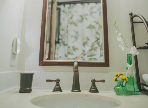 A bathroom sink with a mirror, floral shower curtain, and decorative vases with flowers on the counter.