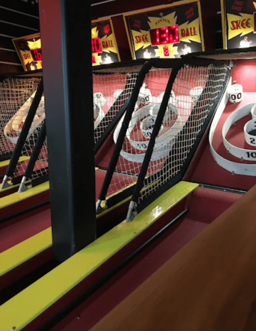 A close-up of a skee ball arcade game with scoring targets and nets, set in a vibrant gaming environment.