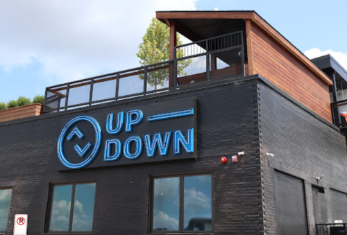 A modern building with a black exterior and a large blue neon sign reading "UP DOWN." A rooftop deck is visible.