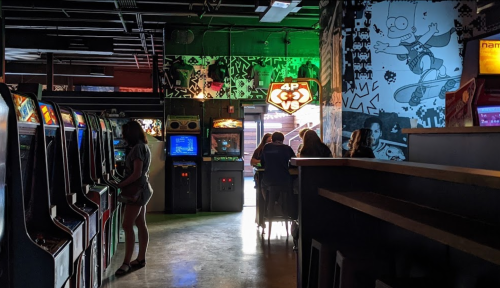 A retro arcade with vintage game machines, colorful walls, and people enjoying games in a lively atmosphere.