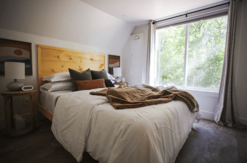 Cozy bedroom with a large window, a bed with pillows and a blanket, and natural light streaming in.