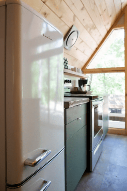 A modern kitchen featuring a white refrigerator, green cabinets, and a window with natural light.