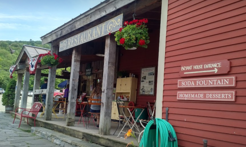 A charming restaurant entrance with a soda fountain sign and hanging flower baskets, set in a rustic red building.