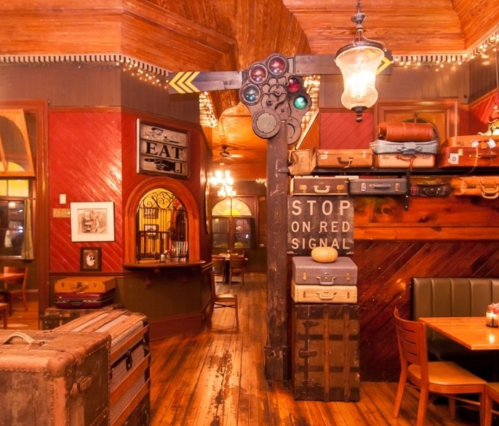 Cozy restaurant interior with vintage decor, including a traffic signal and stacked suitcases, warm lighting, and wooden floors.