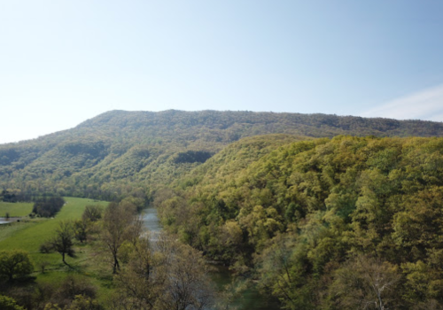 A scenic view of a river winding through lush green hills under a clear blue sky.