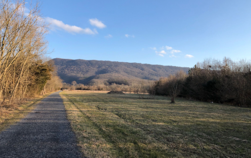 A gravel path leads through a grassy field, with mountains in the background under a clear blue sky.