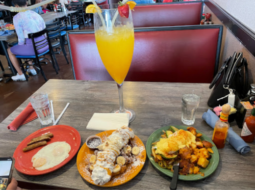 A table with a large drink, breakfast plate with eggs and sausage, and a dessert with bananas and whipped cream.