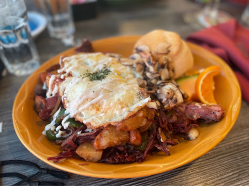A colorful plate featuring a hearty breakfast with eggs, vegetables, and a roll, garnished with an orange slice.