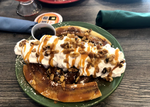 A plate of dessert featuring banana slices topped with whipped cream, caramel drizzle, and chopped walnuts.