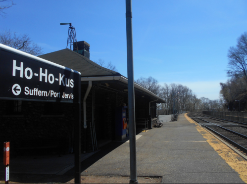 Sign for Ho-Ho-Kus train station with a clear blue sky and empty platform visible.