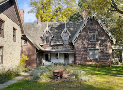 Historic stone house with intricate architecture, surrounded by greenery and a small fire pit in the yard.