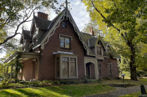 A large, historic house with intricate architecture, surrounded by lush green trees and a clear blue sky.