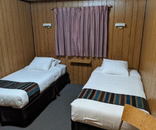 A simple room with two twin beds, wooden paneling, a pink curtain, and a small shelf between the beds.