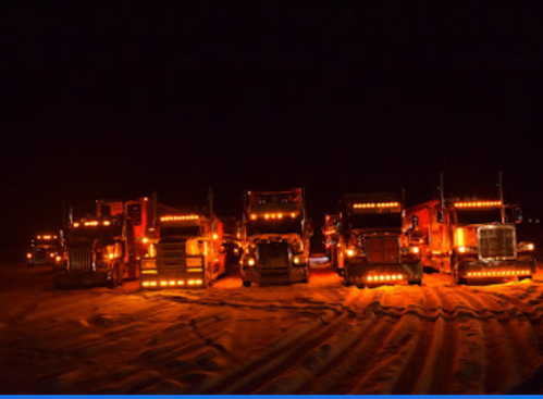 A row of illuminated trucks parked in a snowy landscape at night, glowing with orange lights.