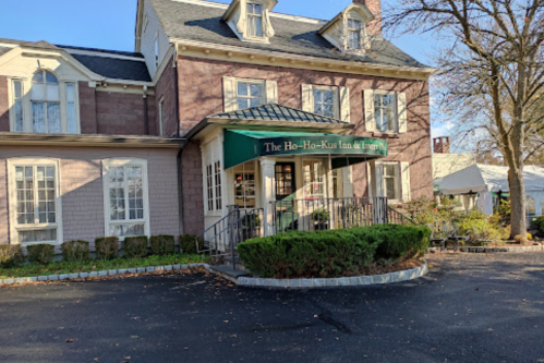 Exterior of the Ho-Ho-Kus Inn & Tavern, featuring a green awning and landscaped entrance on a sunny day.