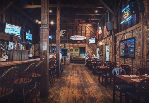 A rustic bar interior with wooden beams, tables, and TVs, creating a cozy atmosphere.