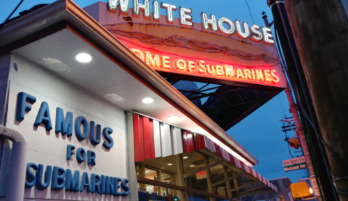 Neon sign for "White House" restaurant, advertising "Famous for Submarines," illuminated at dusk.