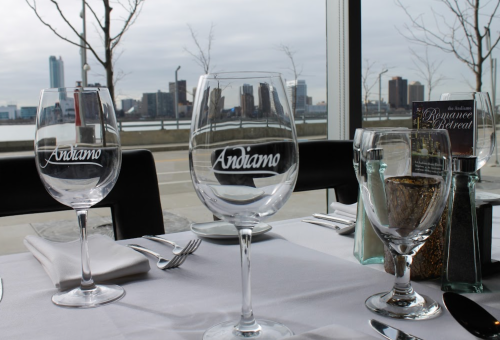 A dining table set with wine glasses and silverware, overlooking a city skyline by the water.