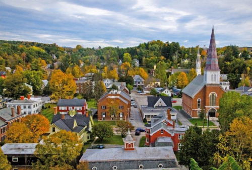 Aerial view of a small town with colorful autumn trees, historic buildings, and a prominent church steeple.