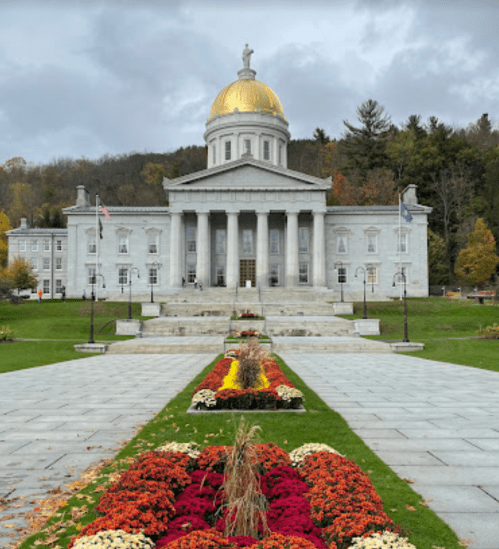 A grand building with a golden dome, surrounded by colorful flower beds and autumn foliage under a cloudy sky.