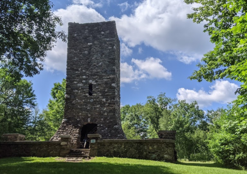 A tall stone tower surrounded by greenery under a partly cloudy sky.