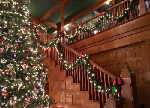 A beautifully decorated Christmas tree beside a wooden staircase adorned with garlands and lights.