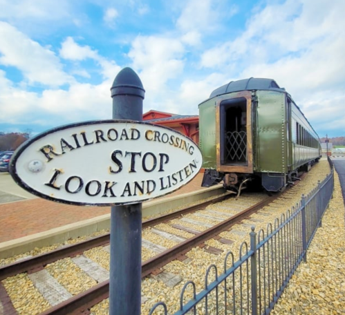 A vintage train car next to a railroad crossing sign that reads "Stop Look and Listen." Blue sky in the background.