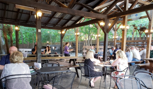 A lively outdoor dining area with wooden beams, tables, and patrons enjoying their meals under warm lights.