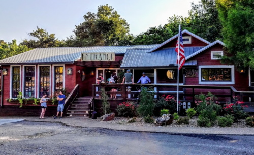 A charming red restaurant with a sign reading "Entrance," surrounded by greenery and flowers, and an American flag.