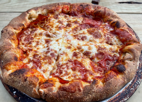 A freshly baked pepperoni pizza with melted cheese and a golden crust, served on a wooden table.