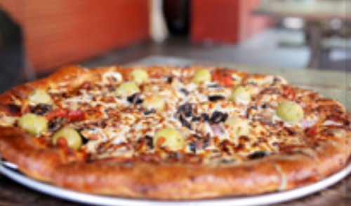 A close-up of a pizza topped with olives, cheese, and various vegetables on a wooden table.