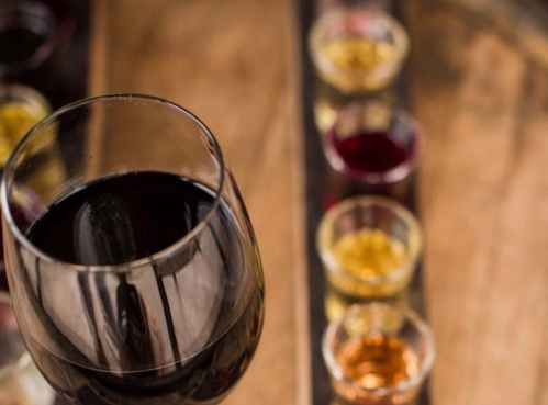 A close-up of a glass of red wine with a flight of colorful spirits in small glasses in the background.