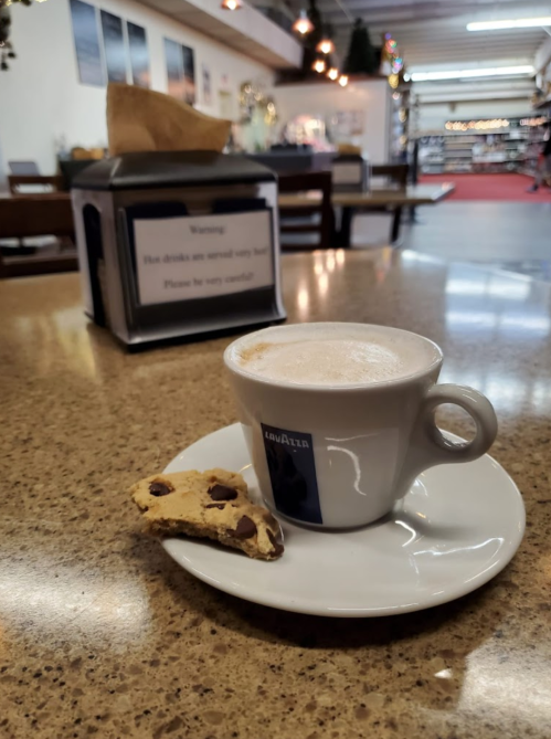 A cup of cappuccino on a saucer with a cookie, placed on a table in a cozy café setting.