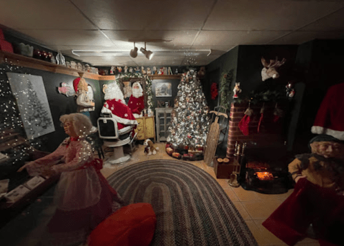 A cozy holiday room decorated with Santa figures, a Christmas tree, and vintage dolls, creating a festive atmosphere.