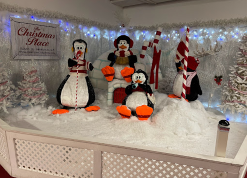 A festive display featuring four penguins in winter attire, an igloo, and candy canes, surrounded by snowy decor.