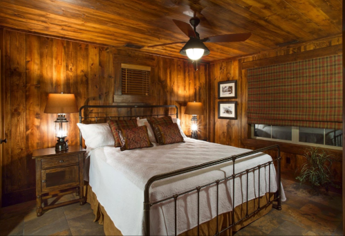 Cozy bedroom with wooden walls, a metal bed frame, warm lighting, and a plaid window shade.