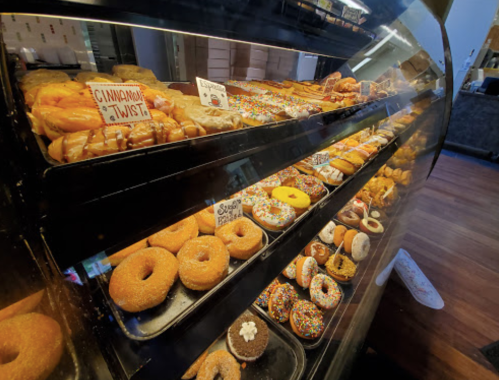 A display case filled with various donuts, including glazed, sprinkled, and cinnamon twist varieties.