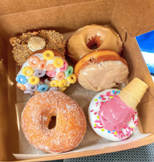 A box of colorful donuts, including a cereal-topped donut, a chocolate frosted donut, and a donut with ice cream.