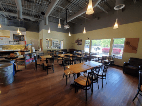 A spacious café interior with wooden tables, chairs, and large windows letting in natural light.