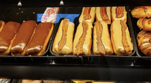 A display of donuts topped with chocolate and bacon, arranged in a bakery case.